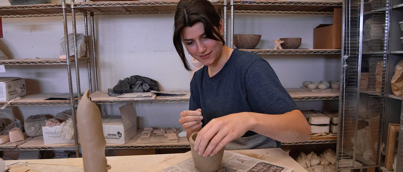 Smiling art student looking at the camera as she paints a ceramic project with glaze