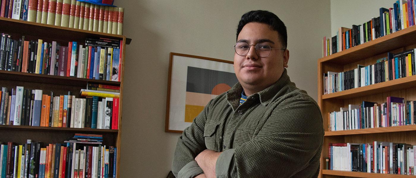 Spanish student with arms crossed standing in front of bookshelves filled with Spanish literature