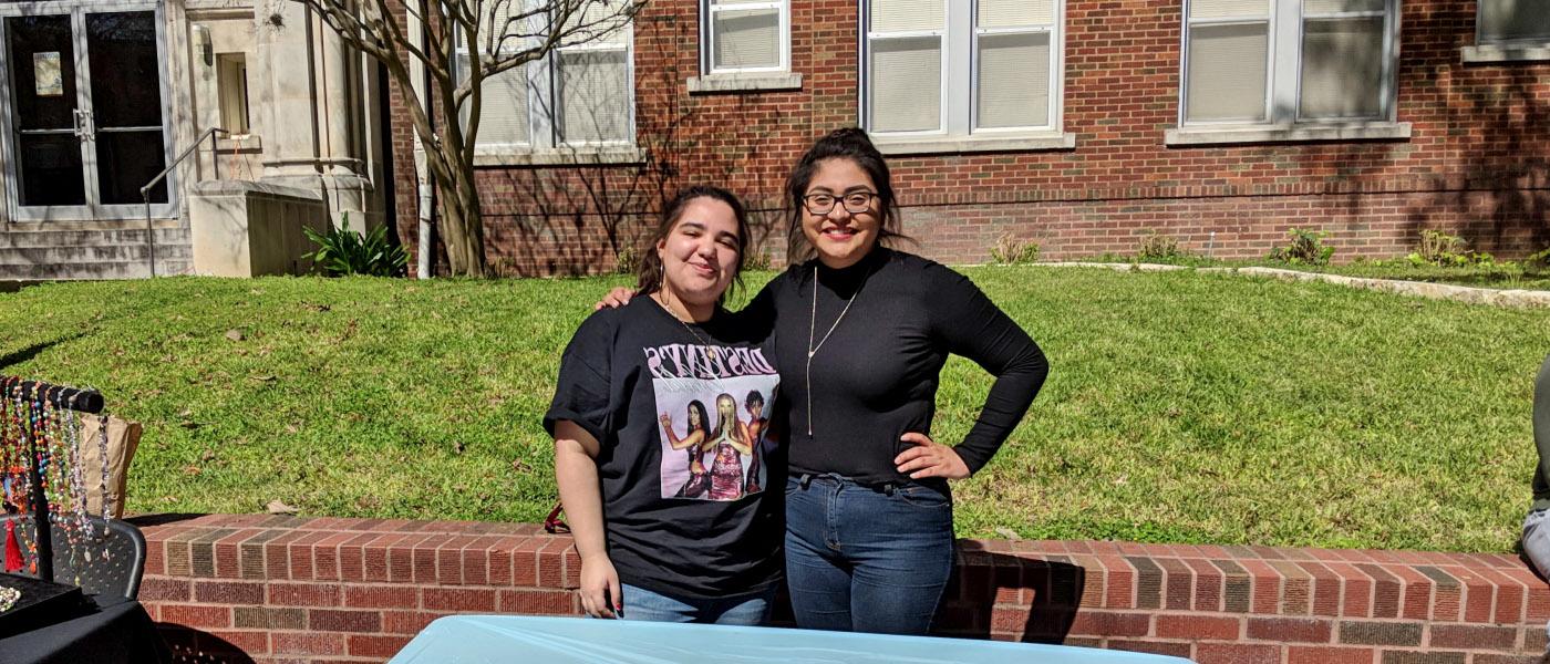 Two smiling women's studies students recruiting members for a club in the courtyard