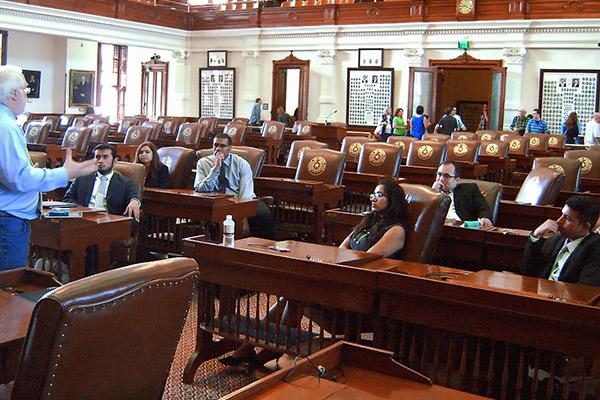 Students sitting in the local house of representatives floor as a professor gives a lesson on the legislative process