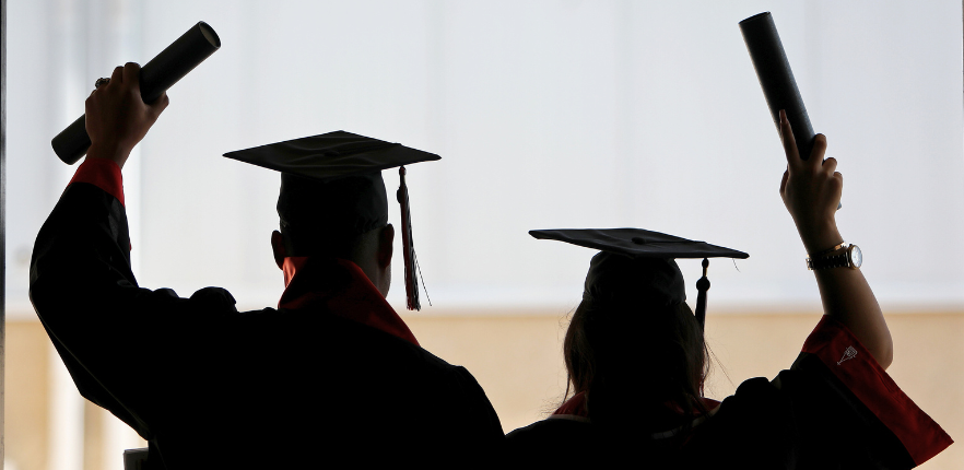 Two UIW graduates facing away from the camera, holding up diplomas in celebration