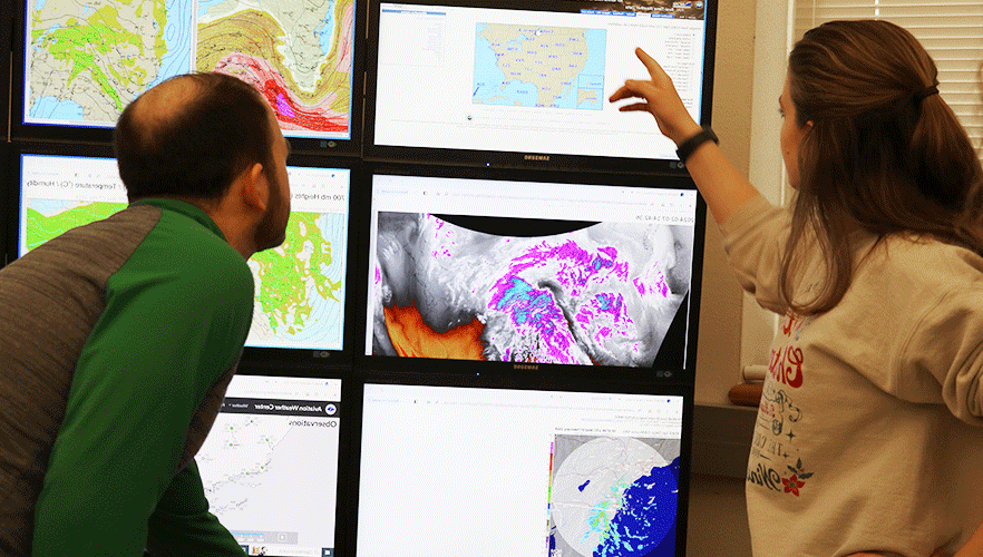 2 meteorology students looking at forecast monitors