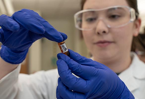 Student in goggles and a lab coat with a vial